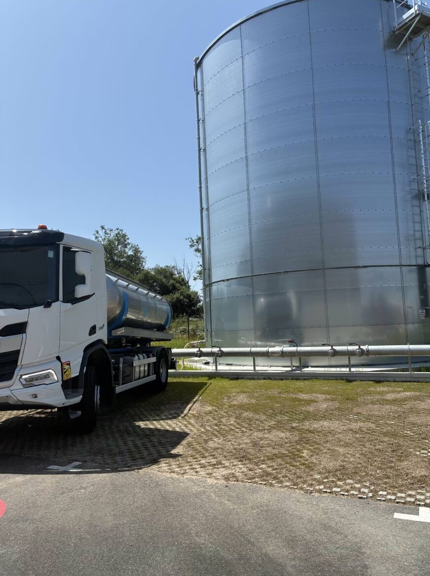Camion-citerne blanc JMGC alimentant une réserve d'eau sur un chantier